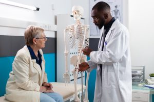 A physician talking to a patient using a model skeleton