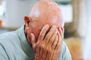 A depressed elderly man covering his face with his hands.